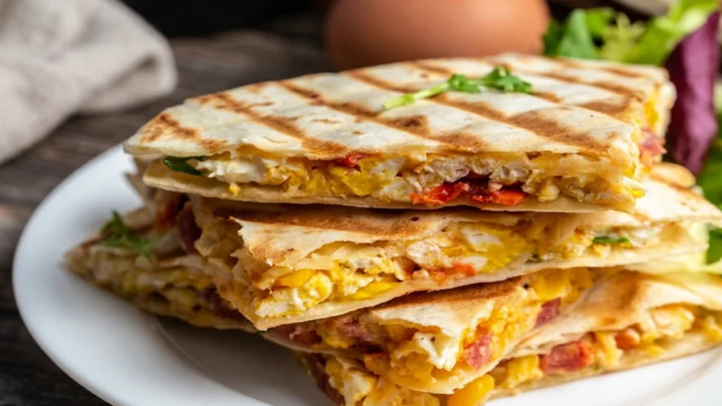 A stack of grilled high-protein Breakfast Quesadilla filled with scrambled eggs, melted cheese, and chorizo on a white plate.