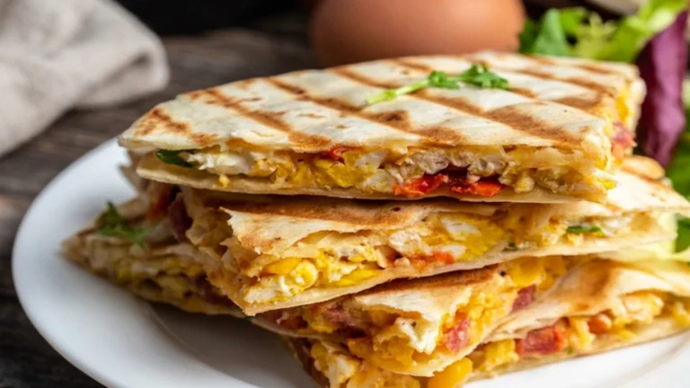 A stack of grilled high-protein Breakfast Quesadilla filled with scrambled eggs, melted cheese, and chorizo on a white plate.