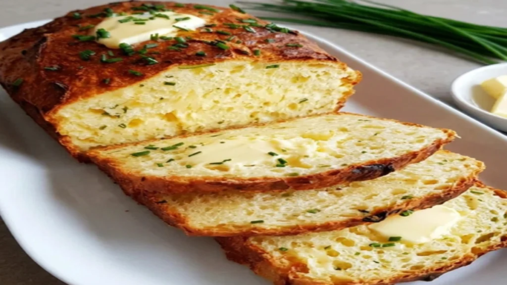 Slices of Easy 2-Ingredient Cottage Cheese Bread topped with melting butter and fresh chives on a wooden board.