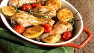 Sheet Pan Chicken and Veggies with roasted chicken potatoes cherry tomatoes and herbs in a baking dish.