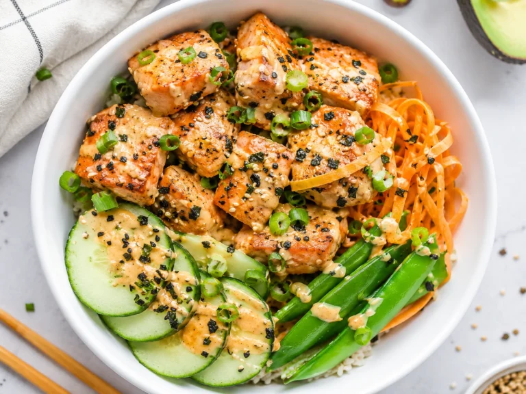 Air Fryer Salmon Bowls served in a white bowl with crispy salmon bites, cucumber slices, snap peas, shredded carrots, green onions, sesame seeds, and creamy sauce over rice.