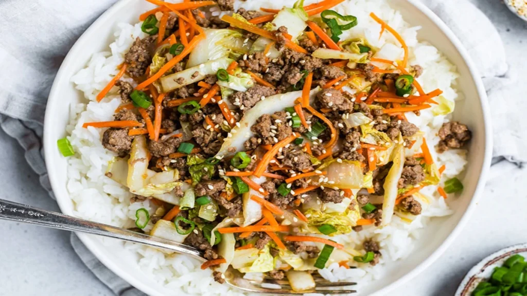 A bowl of white rice topped with a Chinese Ground Beef and Cabbage stir-fry, sprinkled with sesame seeds.