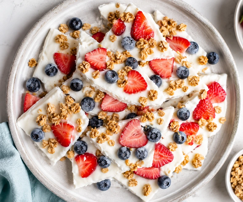 Frozen Greek Yogurt Bark topped with fresh strawberries, blueberries, and crunchy granola on a white serving platter.