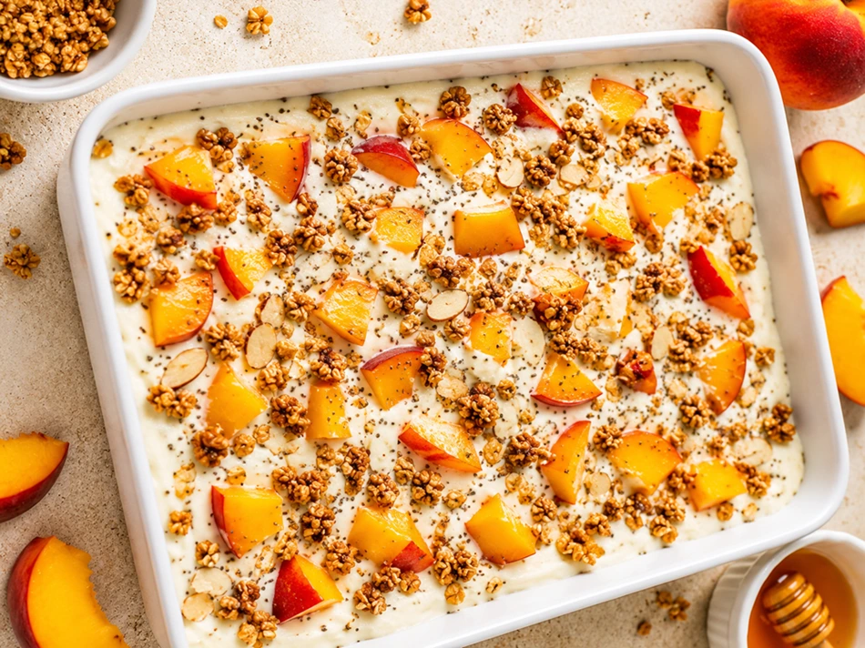 Frozen Yogurt Bark with Peaches and Granola served in a white baking dish topped with fresh peaches, crunchy granola, almonds, and honey.