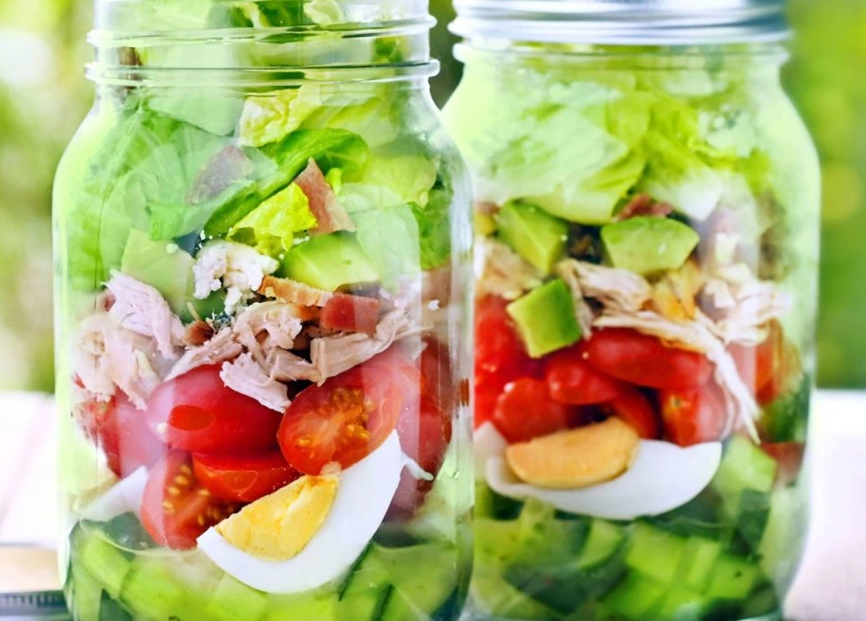 Mason Jar Cobb Salad layered with crisp lettuce, chicken, avocado, cherry tomatoes, cucumber, and hard-boiled eggs in glass mason jars.