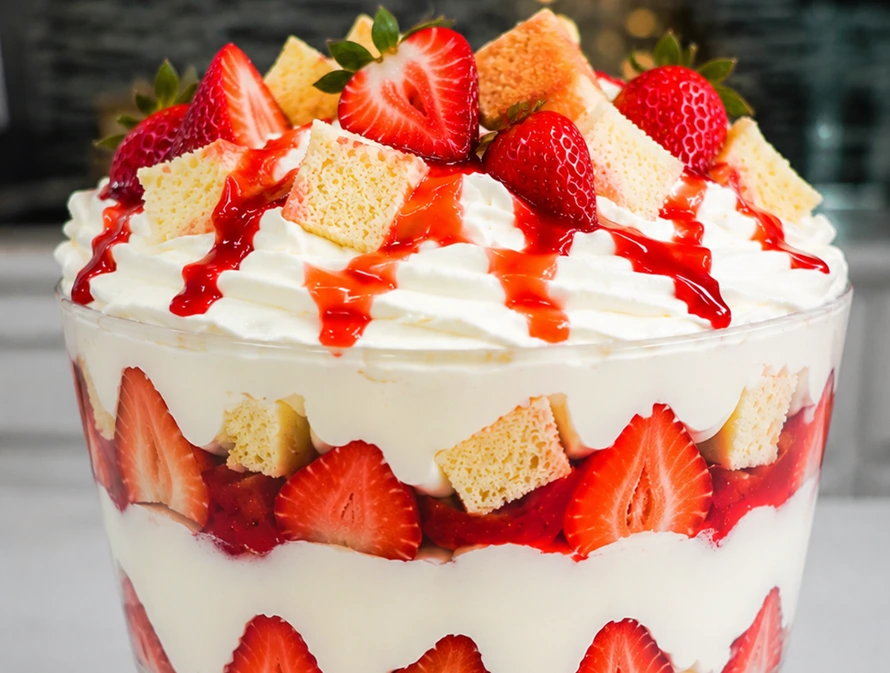 Strawberry Banana Pudding Dream Holiday layered dessert in a glass trifle bowl with fresh strawberries, creamy pudding, whipped topping, and sponge cake cubes.