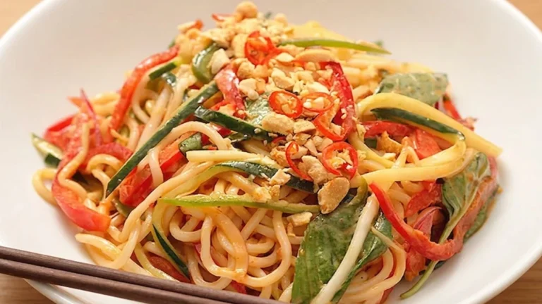 Cold Spicy Peanut Noodle Bowl with fresh vegetables, crunchy peanuts, and chili slices in a white bowl.