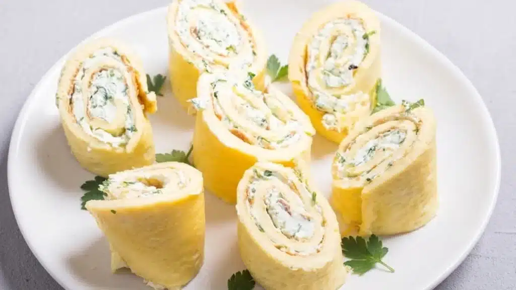 Creamy egg omelette rolls with cream cheese and parsley sliced into pinwheels and served on a white plate.