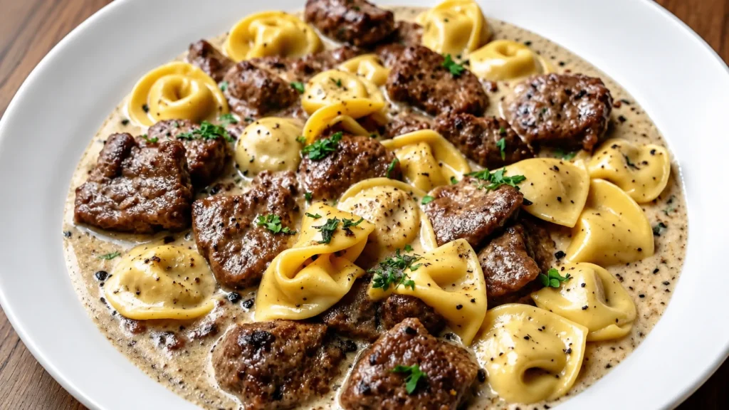 Creamy Garlic Steak Tortellini served in a white bowl with tender steak bites, cheesy tortellini, rich garlic cream sauce, black pepper, and fresh parsley garnish.