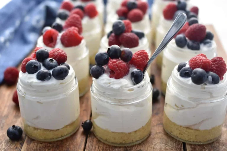 Mini Low-Carb Cheesecake Jars topped with fresh blueberries and raspberries, featuring a creamy keto cheesecake filling and a buttery low-carb crust in glass jars.