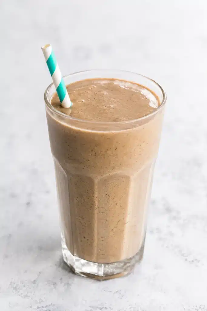 Banana Peanut Butter Coffee Smoothie recipe served in a tall faceted glass with a striped straw, featuring a creamy texture and rich coffee flavor on a light background.