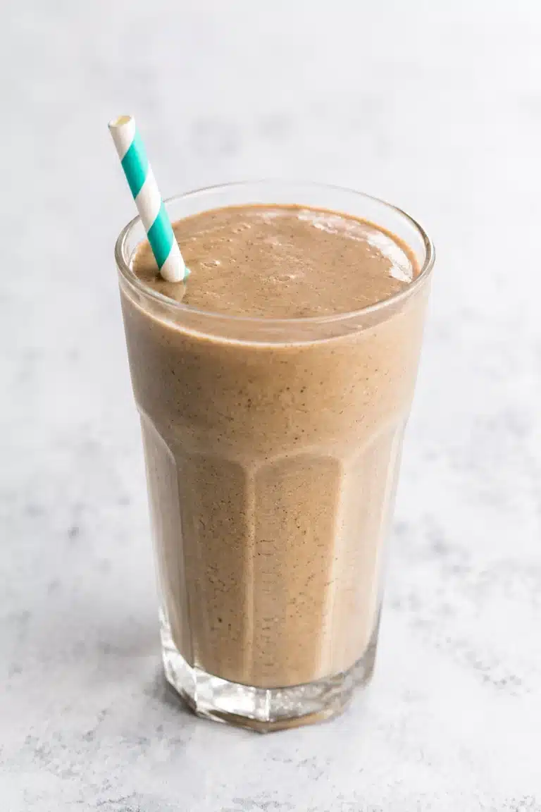 Banana Peanut Butter Coffee Smoothie recipe served in a tall faceted glass with a striped straw, featuring a creamy texture and rich coffee flavor on a light background.
