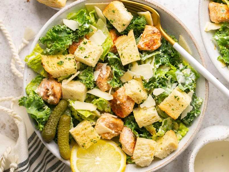Chicken Caesar Meal Prep bowl topped with grilled chicken, crispy croutons, fresh romaine lettuce, kale, shaved Parmesan cheese, and creamy Caesar dressing.