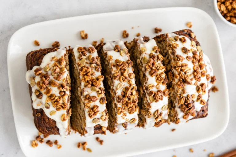 Cottage Cheese Banana Bread sliced on a white platter, topped with creamy glaze and crunchy granola, perfect for a high-protein breakfast or healthy snack.