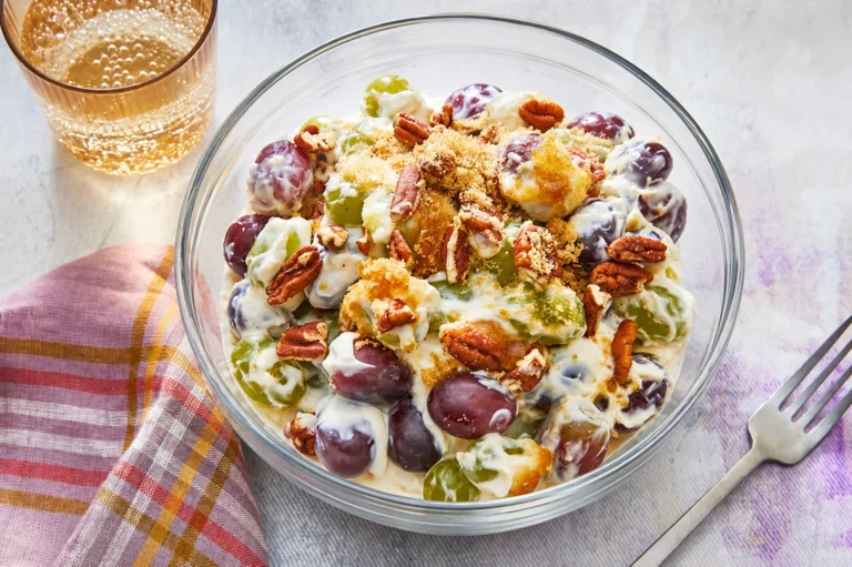 Creamy Grape Salad served in a clear glass bowl with red and green grapes, pecans, and a sweet creamy dressing on a light table setting.