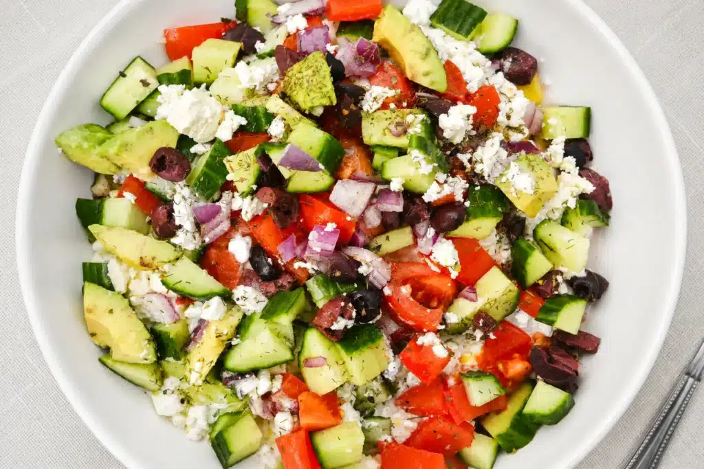Greek Cottage Cheese Protein Bowl topped with cucumber, tomatoes, avocado, red onion, olives, and crumbled feta cheese in a white bowl.
