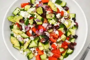 Greek Cottage Cheese Protein Bowl topped with cucumber, tomatoes, avocado, red onion, olives, and crumbled feta cheese in a white bowl.