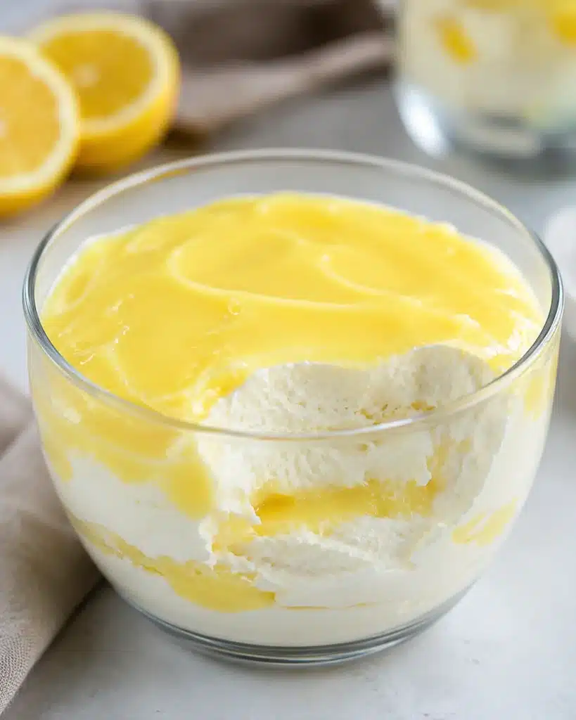 Creamy Lemon Protein Fluff Dessert served in a clear glass bowl with layers of fluffy high-protein lemon filling and smooth lemon topping.