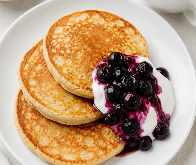 Oatmeal Almond Protein Pancakes served on a white plate with creamy yogurt and a warm blueberry topping for a healthy high-protein breakfast.