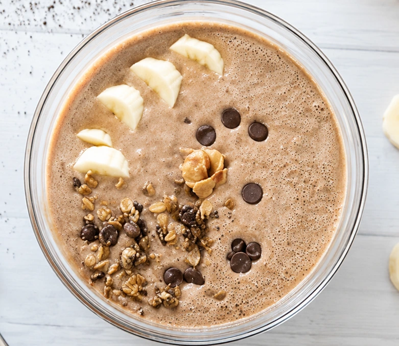 Protein Coffee Smoothie Bowl served in a clear glass bowl and topped with banana slices, granola, nuts, and chocolate chips for a healthy high-protein breakfast.