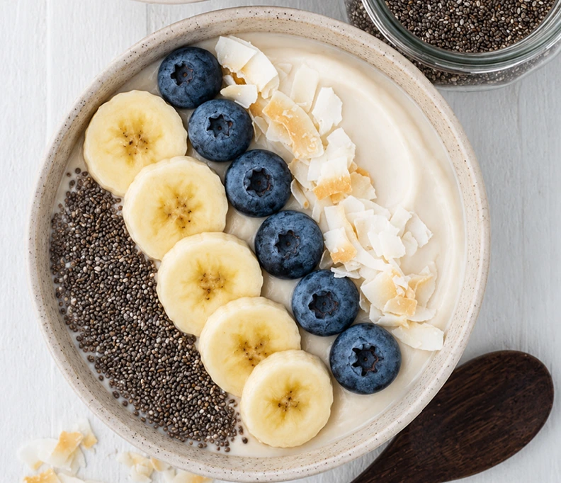 Homemade salted caramel protein pudding topped with banana slices, blueberries, chia seeds, and coconut flakes in a ceramic bowl.