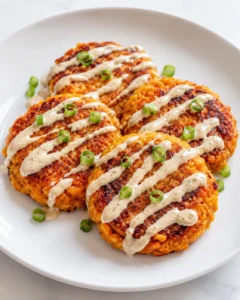 Sweet potato patties with red lentils & tangy tahini dressing served on a white plate, topped with green onions and drizzled with creamy tahini sauce.