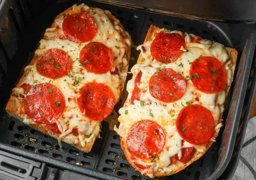Air Fryer French Bread Pizza topped with melted mozzarella, pepperoni, and herbs, cooking in an air fryer basket until crispy and golden.