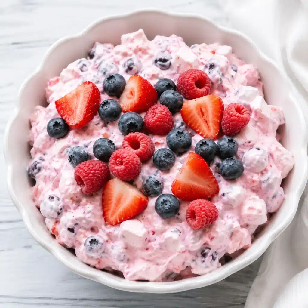 Triple Berry Fluff Dessert served in a white scalloped bowl, topped with fresh strawberries, blueberries, and raspberries for a creamy no-bake summer dessert.
