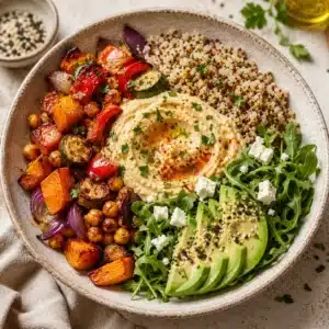 Roasted Veggie & Hummus Grain Bowl with quinoa, roasted sweet potatoes, zucchini, chickpeas, bell peppers, avocado, arugula, feta cheese, and creamy hummus served in a rustic bowl.