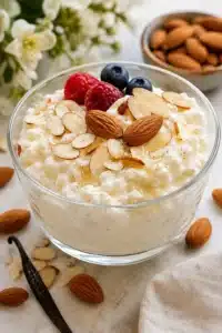 Vanilla Almond Cottage Cheese Dessert topped with sliced almonds, whole almonds, raspberries, blueberries, and vanilla, served in a glass bowl.