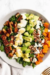 Autumn Cobb Salad with roasted sweet potatoes, avocado, hard-boiled eggs, crispy chicken, feta cheese, pecans, and kale served in a bowl for a healthy fall lunch or dinner.